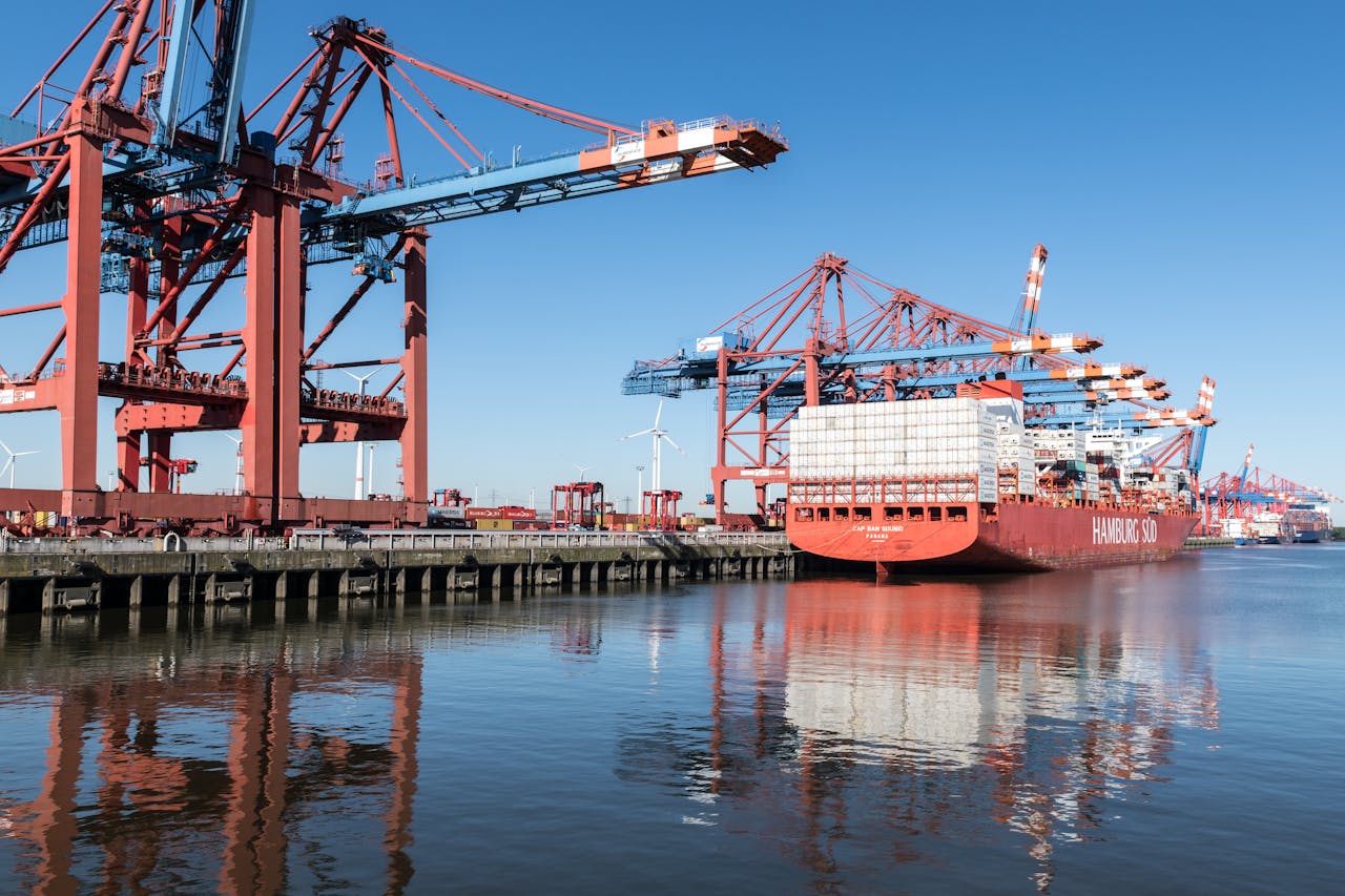 heros-img Container ship at Hamburg port with cranes on a clear day, showcasing industrial operations.